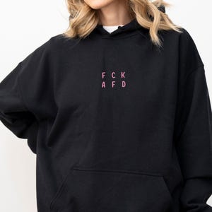 May include: Black hooded sweatshirt with a pink embroidered design that reads "FCK AFD".