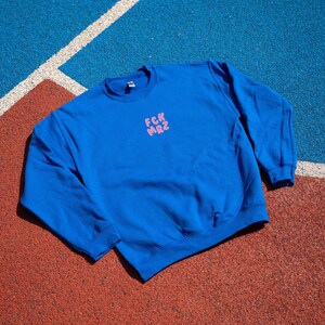 Op de afbeelding: Een koninklijk blauw sweatshirt met een roze afbeelding met de tekst "FCK MRZ" op de voorkant.