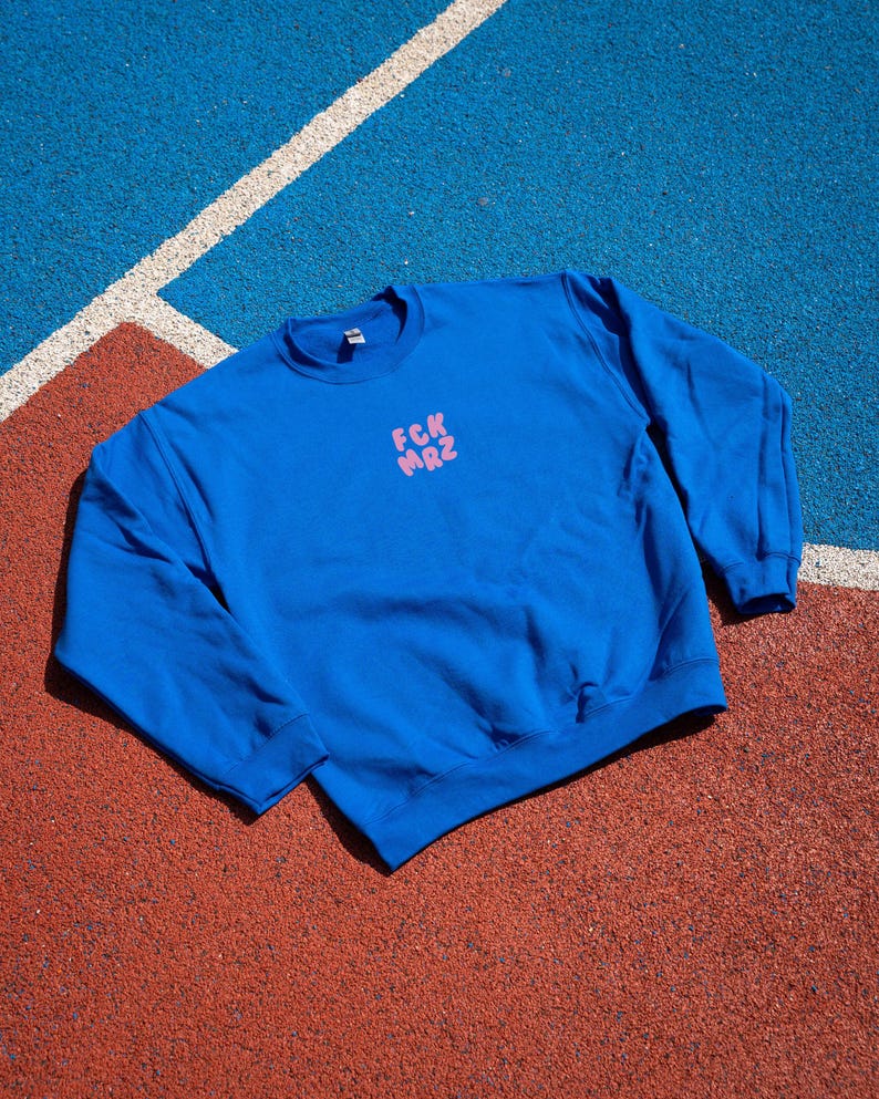 Op de afbeelding: Een koninklijk blauw sweatshirt met een roze afbeelding met de tekst "FCK MRZ" op de voorkant.