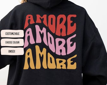 May include: Black hoodie featuring the word "AMORE" in red, pink, and yellow. The word "AMORE" is stacked three times in a retro font. The hoodie has a hood and is made of a soft material.