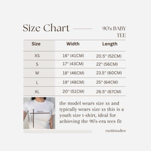 Puede incluir: Tabla de tallas para una camiseta de beb&eacute; de los 90, que muestra las medidas en pulgadas y cent&iacute;metros para las tallas XS, S, M, L y XL. La tabla muestra el ancho y la longitud de cada talla. La modelo lleva la talla XS.
