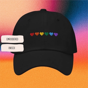 Könnte beinhalten: Schwarze Baseballkappe mit gestickten Regenbogenherzen. Die Kappe hat einen gebogenen Schirm und ein Design mit sechs Herzen in Rot, Orange, Gelb, Grün, Blau und Lila. Die Texte "EMROIDERED" und "UNISEX" befinden sich auf der linken Seite.