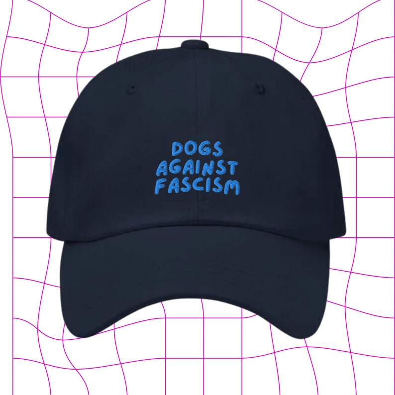 Może przedstawiać: Czapka bejsbolowa w kolorze granatowym z haftem "DOGS AGAINST FASCISM" w jasnoniebieskim kolorze.