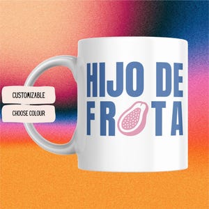 Könnte beinhalten: Weiße Keramik-Tasse mit gebogenem Henkel. Die Tasse zeigt den Text "HIJO DE FROTA" in Blau, mit einer rosa Papaya-Illustration. Die Wörter "CUSTOMIZABLE" und "CHOOSE COLOUR" stehen auf einem separaten Etikett.