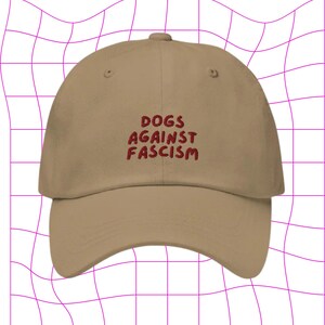 Może przedstawiać: Beżowa czapka z daszkiem z haftem "DOGS AGAINST FASCISM" w kolorze czerwonym z przodu.