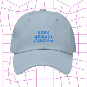 Może przedstawiać: Jasnoniebieska czapka z daszkiem z haftem "DOGS AGAINST FASCISM" w kolorze niebieskim.