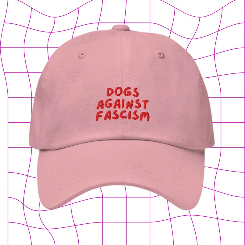 Może przedstawiać: R&oacute;żowa czapka z daszkiem z haftem "DOGS AGAINST FASCISM" w kolorze czerwonym.