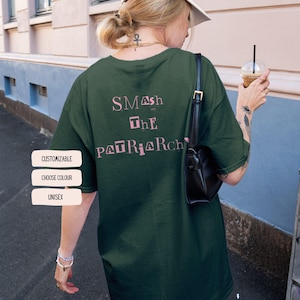 Könnte beinhalten: Dunkelgrünes Unisex-T-Shirt mit dem Text "SMASH THE PATRIARCH" in Rosa. Das Shirt hat eine lockere Passform. Das Bild zeigt auch drei weiße rechteckige Knöpfe mit den Wörtern "CUSTOMIZABLE", "CHOOSE COLOUR" und "UNISEX".
