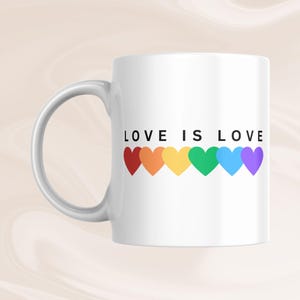 May include: White ceramic mug with the text "LOVE IS LOVE" above a row of six colorful hearts in the colors of the rainbow. The mug has a curved handle and is suitable for hot or cold beverages.