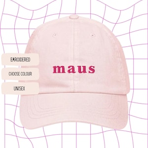 Può includere: Cappellino da baseball rosa chiaro con la parola "maus" ricamata in rosa più scuro. Il cappellino ha una visiera curva e un design a sei pannelli. Lo sfondo è una griglia bianca con linee rosa. Testo a sinistra: "EMBROIDERED", "CHOOSE COLOUR" e "UNISEX".