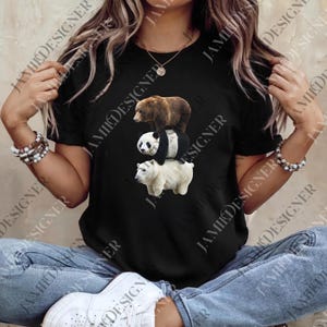 May include: Black t-shirt featuring a stacked bear design: a brown bear on top, a panda in the middle, and a polar bear at the bottom. The shirt is worn by a person wearing blue jeans and white sneakers.