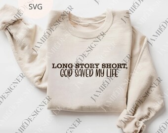 Puede incluir: Una sudadera color crema con el texto "LONG STORY SHORT, GOD SAVED MY LIFE" en fuente marrón oscuro. La sudadera está doblada cuidadosamente, con las mangas enrolladas. La imagen también incluye "PNG + SVG" en la esquina superior izquierda.
