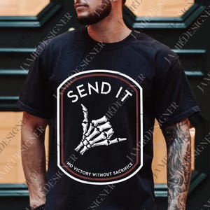 May include: Black t-shirt featuring a white and brown graphic. The graphic includes the text "SEND IT" above a skeleton hand making a shaka sign. The text "NO VICTORY WITHOUT SACRIFICE" is below the hand.