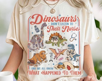 Puede incluir: Una camiseta de color crema con un estampado gráfico que incluye el texto "Dinosaurs didn't listen to their nurses and we all know what happened to them." El diseño muestra ilustraciones de varios dinosaurios con suministros médicos.