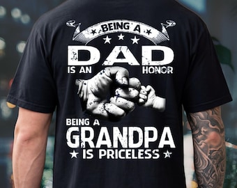 Puede incluir: Una camiseta negra de manga corta con un gráfico blanco de un puño adulto chocando con el puño de un niño. El texto dice: BEING A DAD IS AN HONOR, BEING A GRANDPA IS PRICELESS. El diseño incluye estrellas y elementos de pancarta en blanco.