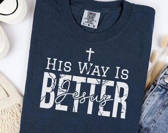 May include: Navy blue t-shirt with the text "HIS WAY IS BETTER Jesus" in white. The shirt has a crew neck and short sleeves. The shirt is made of a soft, comfortable material.