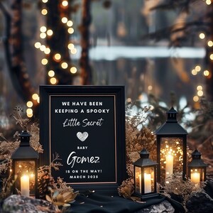 以下が含まれることがあります： 黒い額縁の黒板に、白い文字で「We have been keeping a spooky little secret. Baby Gomez is on the way! March 2025」と書いてある妊娠の発表。看板は、灯りがともった黒い提灯と、素朴な森の背景に囲まれている。