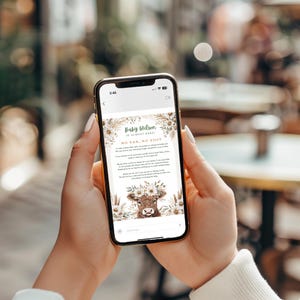 Könnte beinhalten: Ein Smartphone zeigt eine Babyparty-Einladung mit dem Text "Baby Wilson ist fast da!" und "Kein Vax, kein Besuch". Die Einladung zeigt eine Kuh-Illustration mit floralen Akzenten in einer rustikalen, neutralen Farbpalette. Das Telefon wird von einer Person gehalten.