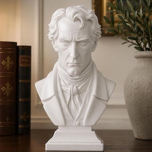 Peut inclure: Buste blanc d'un homme avec des traits faciaux détaillés et des cheveux ondulés. La sculpture est posée sur un socle rectangulaire. L'arrière-plan comprend des livres et un vase, créant une ambiance classique.