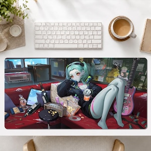 May include: A rectangular desk mat featuring an anime-style illustration of a character with light blue hair and skin, wearing a black jacket, lounging on a red sofa. The scene includes a pink electric guitar, bottles, snacks, and electronic devices.