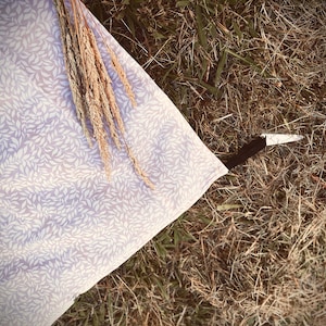 May include: A light purple fabric with a white leaf pattern is partially visible, along with dried wheat stalks. A small knife with a black handle and white blade rests on the grass.