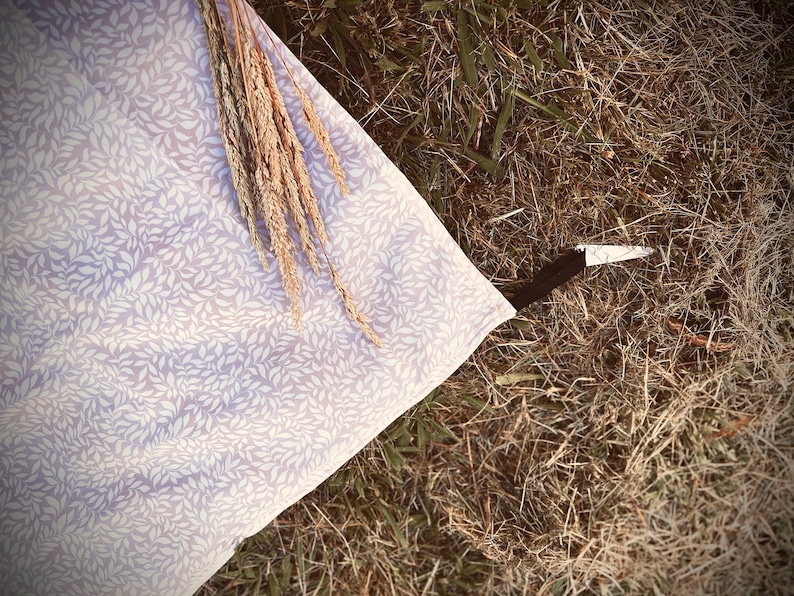 May include: A light purple fabric with a white leaf pattern is partially visible, along with dried wheat stalks. A small knife with a black handle and white blade rests on the grass.