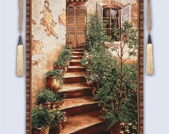 May include: A tapestry depicting a sunlit Italian courtyard scene. A stone staircase leads up to a wooden door and window, flanked by potted plants. The artwork features warm earth tones and a textured, aged appearance, with decorative tassels.