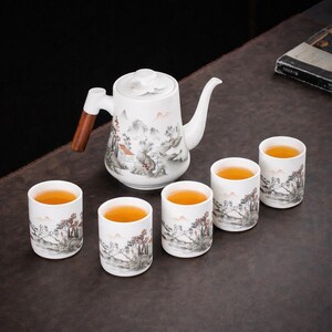 May include: A white ceramic tea set with a teapot featuring a wooden handle and a floral lid, alongside five matching cups. Each piece is decorated with a landscape painting in grey, brown, and red, filled with tea.