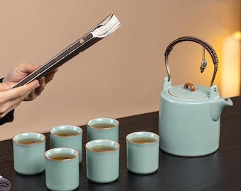 May include: A light blue ceramic tea set with six matching cups, a teapot, and a book. The teapot has a brown handle and a small charm. The cups and teapot are filled with tea.