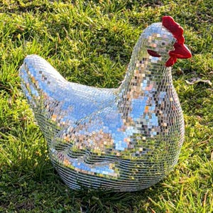 May include: A disco ball chicken sculpture, covered in mirrored tiles, reflecting light. The chicken has a red comb and wattle, and is set on green grass. A unique and eye-catching decorative item.