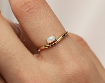 Puede incluir: Un anillo de oro con una piedra de ópalo blanco. El anillo tiene una banda curva.