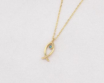 Puede incluir: Un collar de cadena dorada con un pequeño colgante de pez con un ojo de piedra preciosa azul.