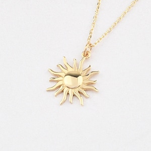 May include: A gold necklace with a sun pendant. The pendant is a simple design with a round center and rays extending out.