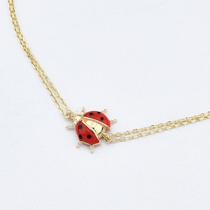May include: A delicate gold chain bracelet featuring a red and black ladybug charm. The bracelet is made of two fine chains and has a lobster clasp fastening.