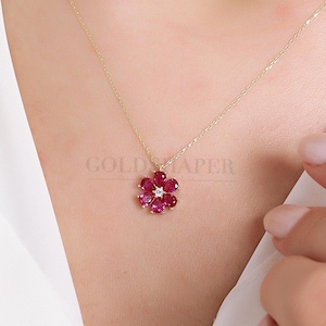 May include: A gold chain necklace with a red ruby flower pendant. The flower has a small diamond in the centre.