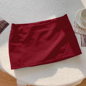 Pu&ograve; includere: Una minigonna tinta unita rosso scuro caratterizzata da un design semplice a taglio dritto con un orlo pulito. Il capo &egrave; realizzato in un tessuto liscio e opaco che mantiene una tonalit&agrave; cremisi profonda e uniforme su tutta la superficie.
