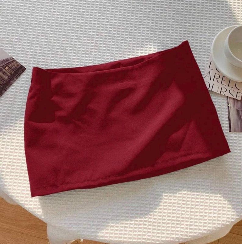 Pu&ograve; includere: Una minigonna tinta unita rosso scuro caratterizzata da un design semplice a taglio dritto con un orlo pulito. Il capo &egrave; realizzato in un tessuto liscio e opaco che mantiene una tonalit&agrave; cremisi profonda e uniforme su tutta la superficie.