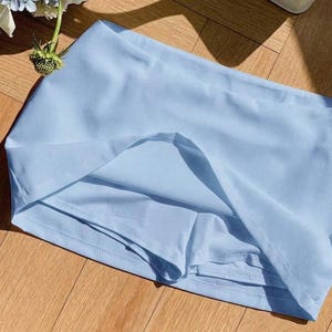 Pu&ograve; includere: Una gonna pantalone color azzurro chiaro realizzata in tessuto liscio a tinta unita, dotata di un'ampia fascia in vita e di pantaloncini integrati sotto il pannello della gonna. Il capo ha un design semplice con cuciture visibili sull'orlo.