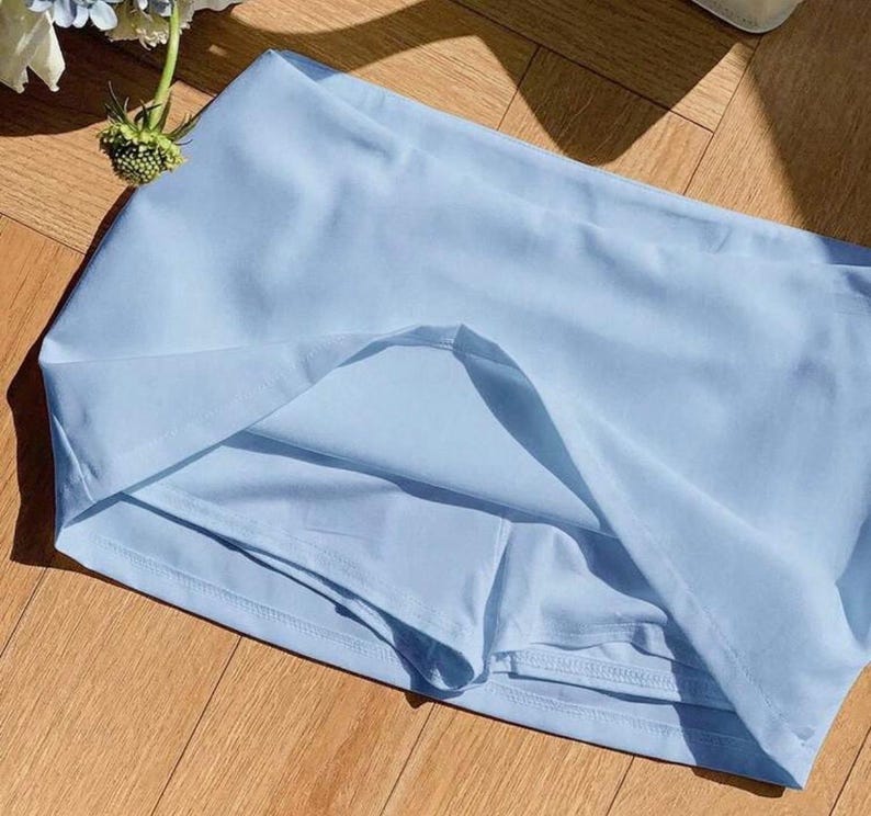 Pu&ograve; includere: Una gonna pantalone color azzurro chiaro realizzata in tessuto liscio a tinta unita, dotata di un'ampia fascia in vita e di pantaloncini integrati sotto il pannello della gonna. Il capo ha un design semplice con cuciture visibili sull'orlo.
