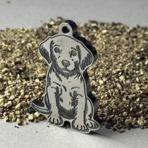 May include: A silver charm in the shape of a sitting puppy. The puppy is outlined in black and has a detailed face.