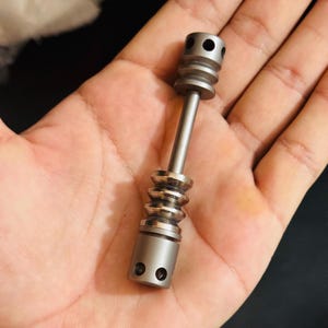 May include: A silver metal tool with a cylindrical body and a rounded top. The tool has a series of ridges along the body and a small hole at the top.