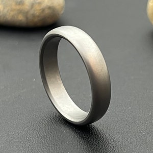 May include: A simple, brushed silver wedding band. The band is smooth and has a slightly rounded edge.