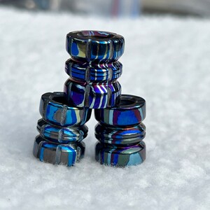 May include: A stack of four blue and purple patterned metal fidget rings. The rings are stacked on top of each other, with the top ring being the smallest and the bottom ring being the largest.