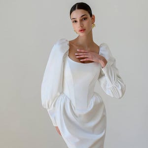 Elegante minivestido de novia blanco con mangas largas voluminosas y corpiño estructurado, perfecto para looks nupciales o formales.
