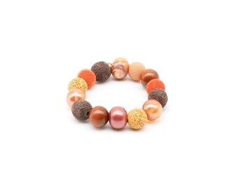 May include: A bracelet made of brown, orange, and beige beads. The beads are of various sizes and textures, including smooth, textured, and speckled.