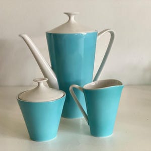Könnte beinhalten: Ein Vintage-Kaffee-Set aus türkisfarbener und weißer Keramik. Das Set umfasst eine hohe Kaffeekanne mit Deckel, eine Zuckerdose mit Deckel und einen Sahnekännchen. Die Teile haben ein schlankes, modernes Design aus der Mitte des Jahrhunderts.