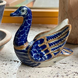 Pode incluir: Uma figurinha de cisne de cerâmica azul e marrom com detalhes intrincados. O cisne tem um pescoço longo e asas estendidas.