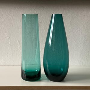 May include: Two teal glass vases, one tall and cylindrical, the other shorter and teardrop shaped.