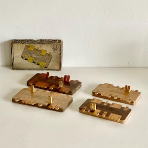 Könnte beinhalten: Ein Vintage-Holzspielset mit vier rechteckigen Spielbrettern und einer Schachtel. Die Bretter sind aus verschiedenen Holztönen gefertigt und haben kleine Stifte. Die Schachtel hat ein gedrucktes Design mit dem Namen des Spiels.