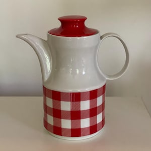 Könnte beinhalten: Eine weiße Keramik-Milchkanne mit rotem Deckel und rotem und weißem Karomuster.